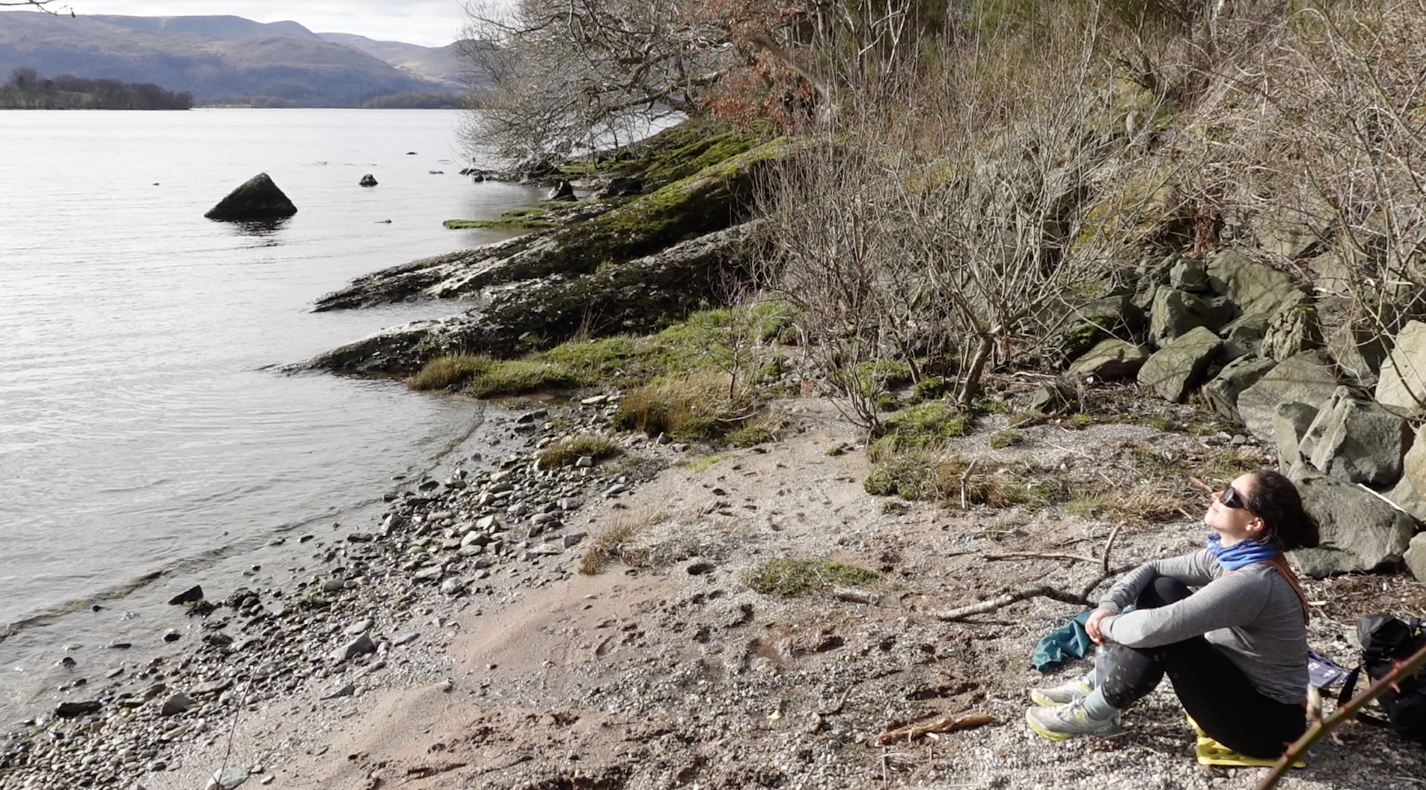 Chloe sitting and resting beside the West Highland Way, taking a mindful break while overlooking the surrounding hills and landscape near Loch Lomond.