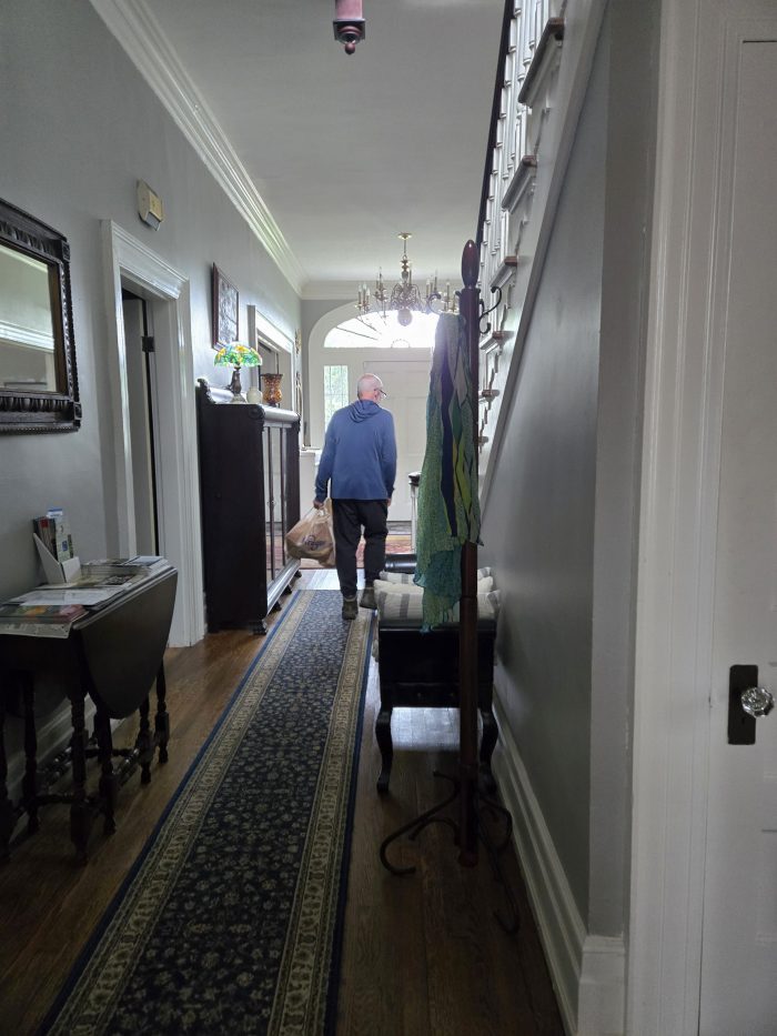 Man walking in hall of historic house with antique carpets and carved stairwell