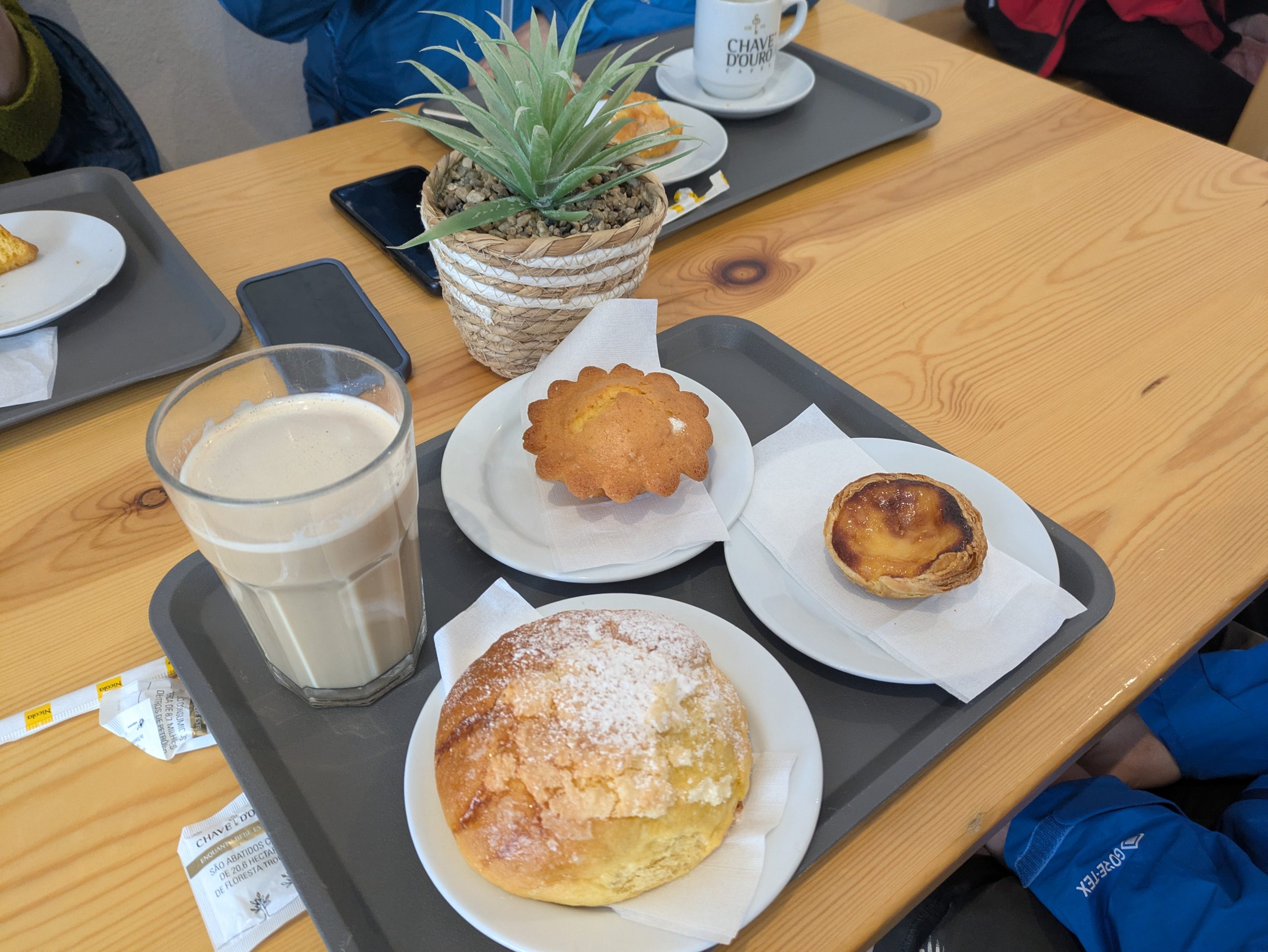 A galão (Portuguese Latte) and a plate of assorted cakes, including a golden whip cake, sitting on an outdoor coffee table.