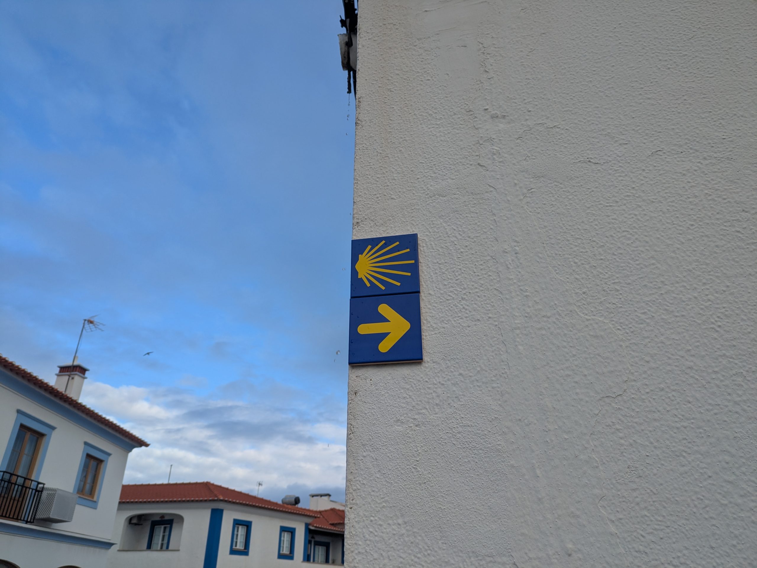 A shell marker of Camino de Santiago Amarillo on a wall in a Portuguese town, pointing out the route of the road through the city.