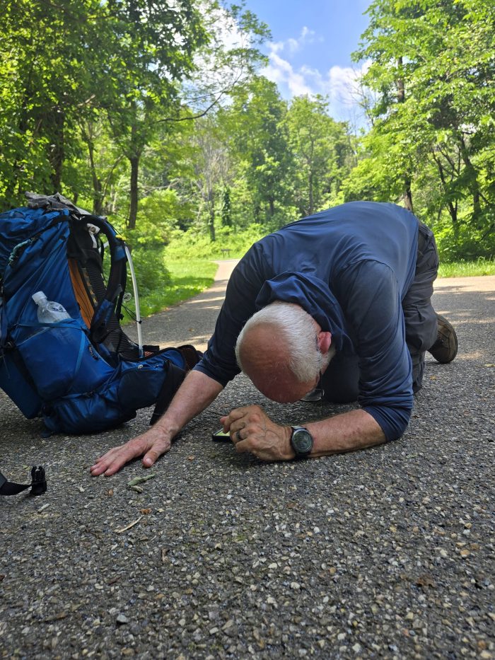 Man in pavement next to the backpack in cat yoga posture.