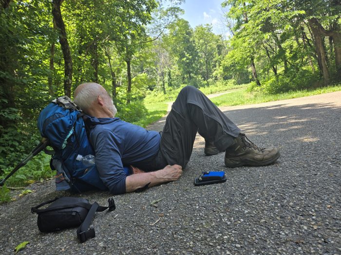 Male backpack sitting on the pavement reclining against the backpack 