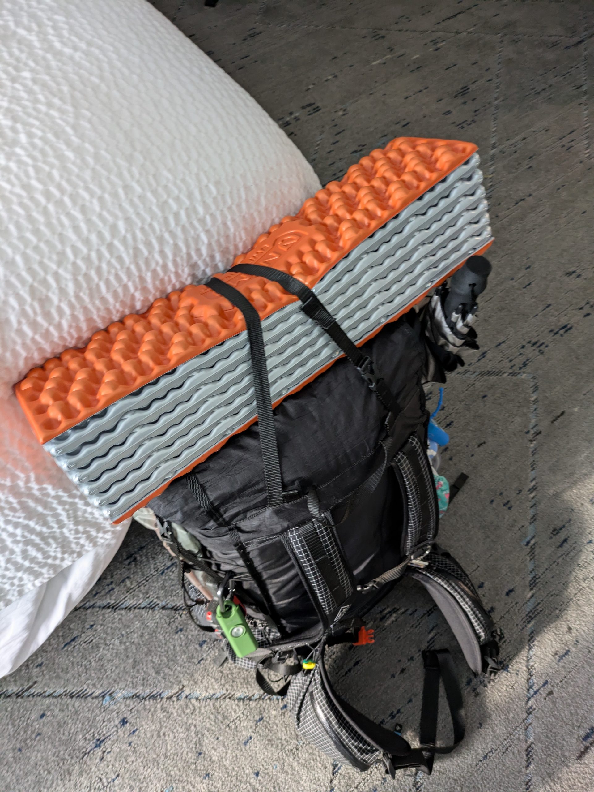 A hiker's black backpack with orange sleeping pad on top.