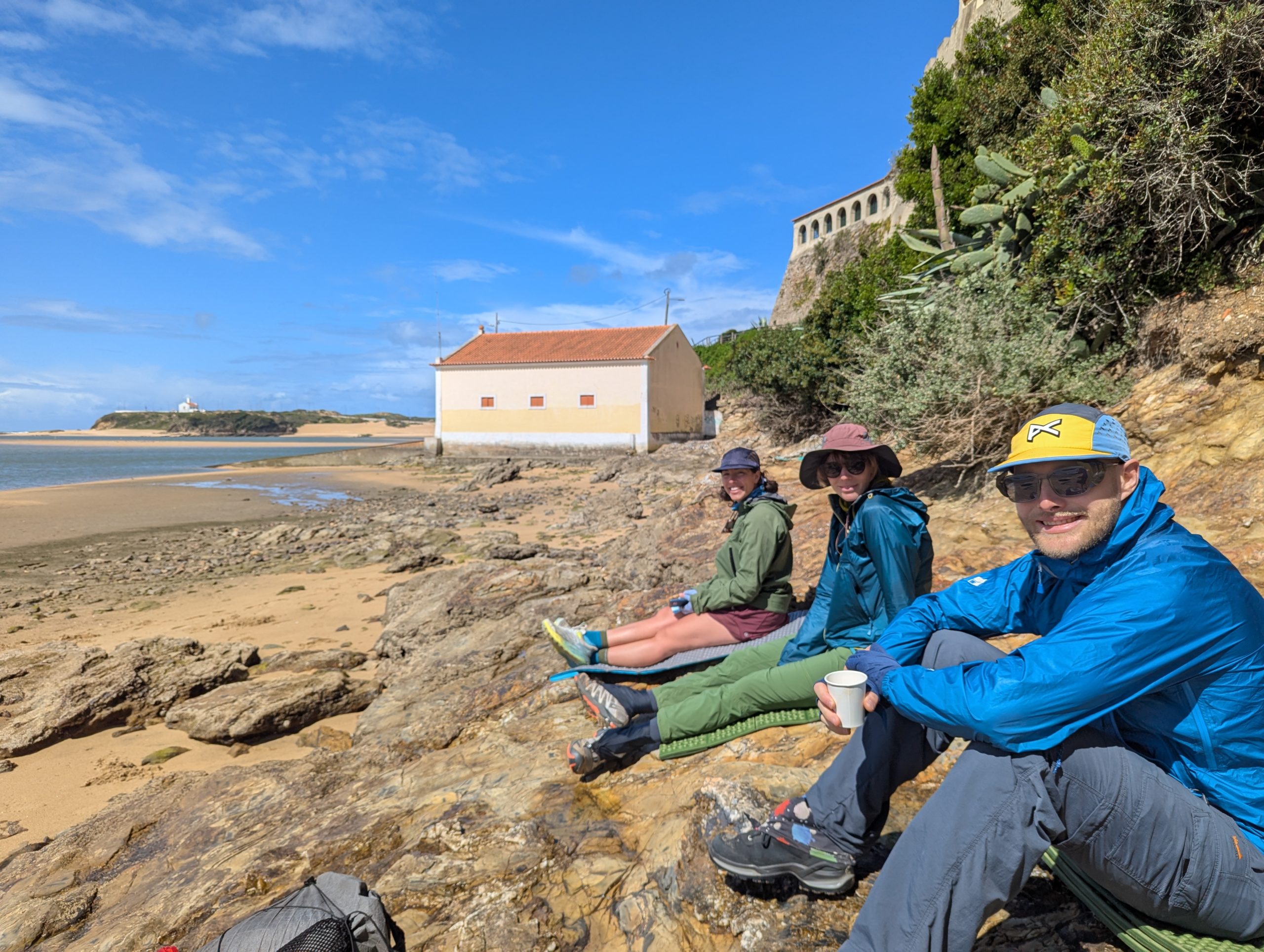 Tres excursionistas sellados en la playa de arena al sol, esperando que el ferry cruce el río para hacer un día.