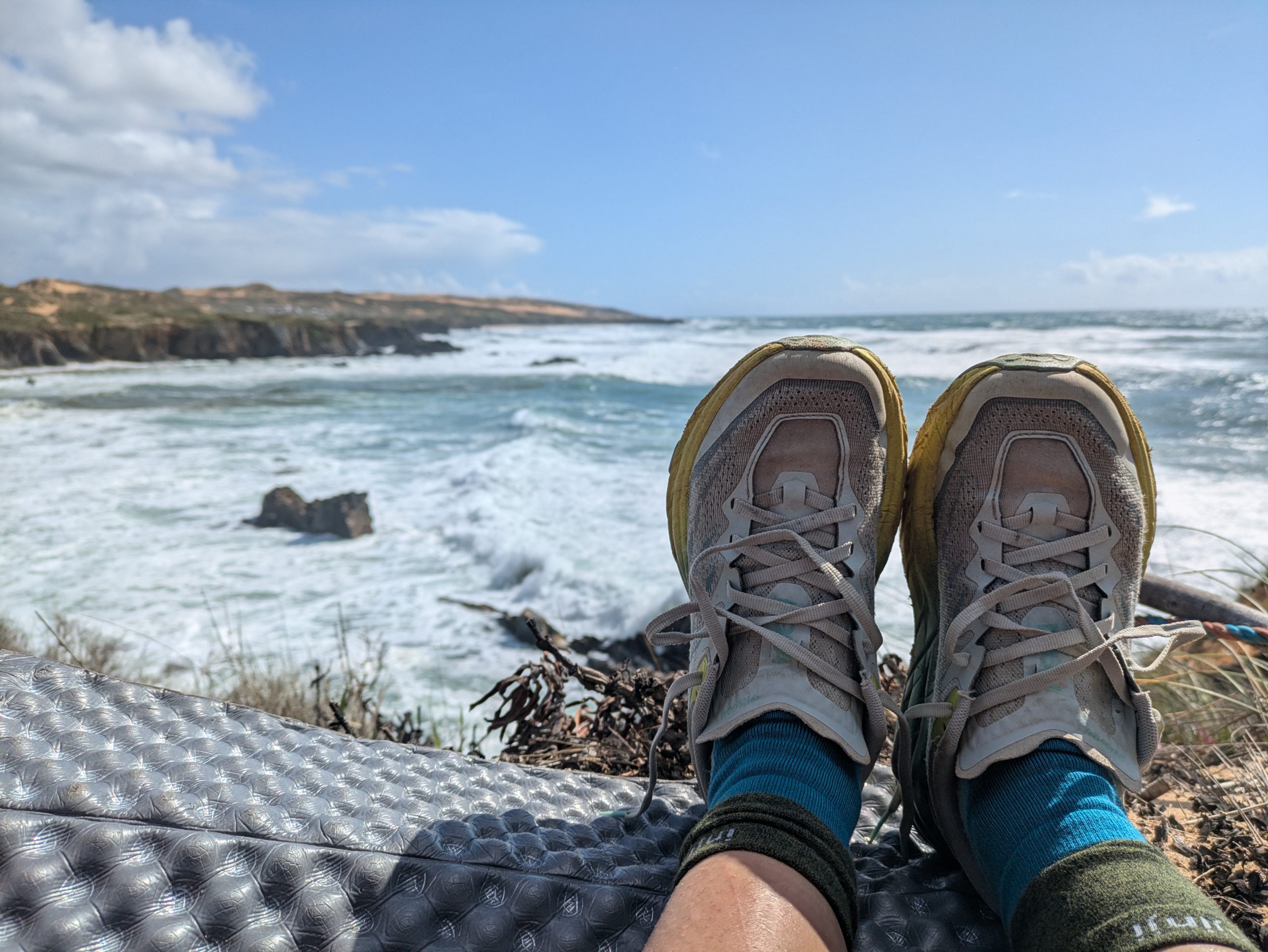 Las piernas y zapatos de excursionistas en las vistas cuando se encuentran en el acantilado del Océano Atlántico en carreteras de pescadores portuarios.