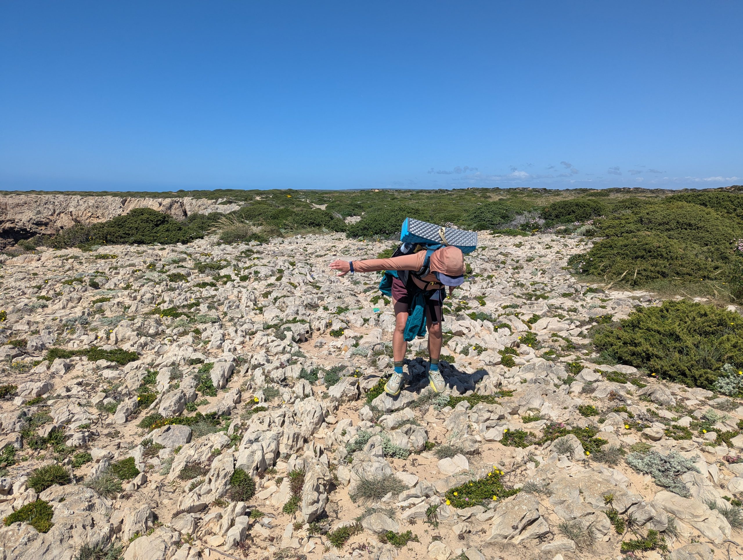 Chloe balancing in half step in rocky terrain, arms to balance, walking along the path of fishermen near Sagres, Portugal.