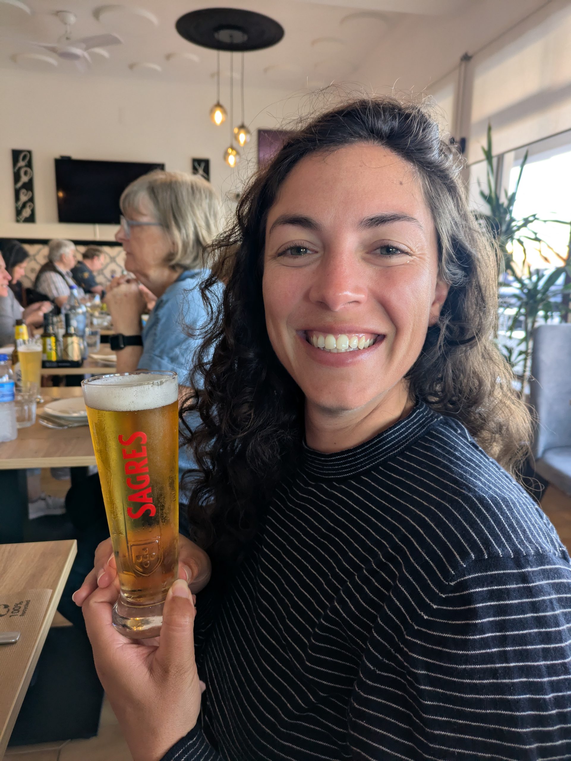 The cold sagres beer sustained against a backdrop of the ocean and cliffs in Sagres, Portugal, celebrating the end of the hiker day of a fishing path.