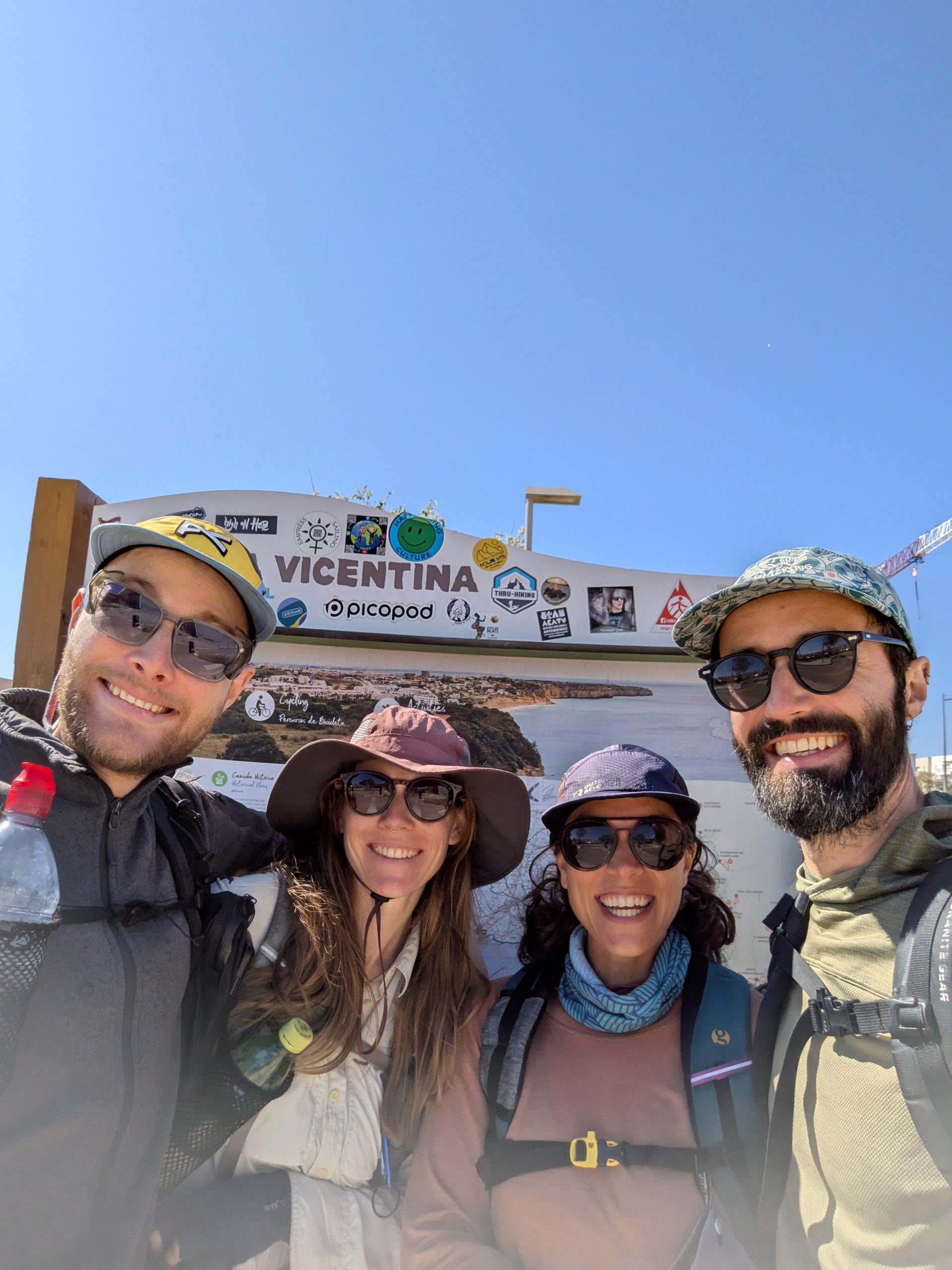 Four hikers smiling together on the terminal of the Path of the Fishermen in Lagos, Portugal, after completing their trip