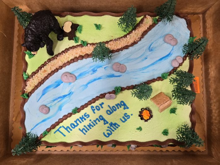 decorated sheet cake with bear, tent, and stream with message saying thanks for hiking along with us.