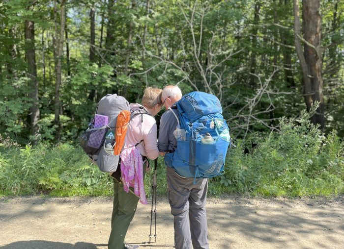 man and woman backpackers, as seen from behind, with their heads inclined to each other.