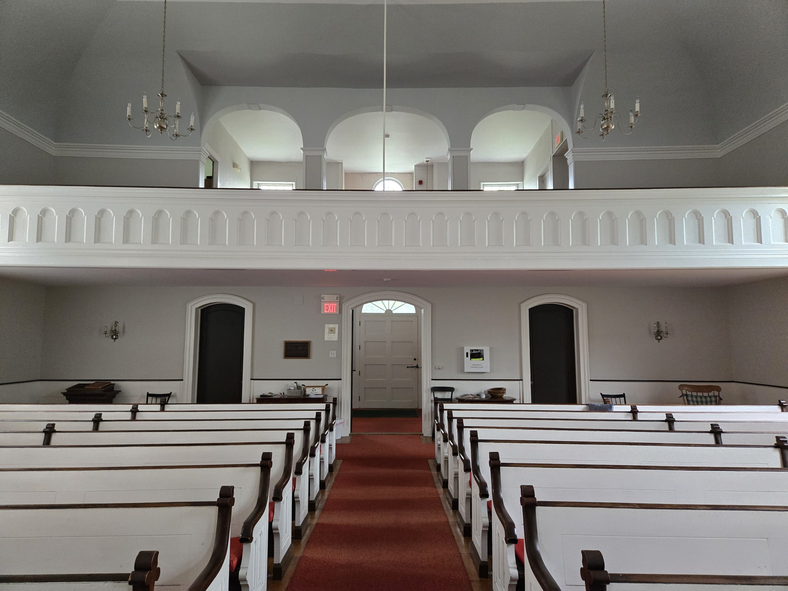Interior of a 1840 new England church displaying white pews and walls and a choir loft
