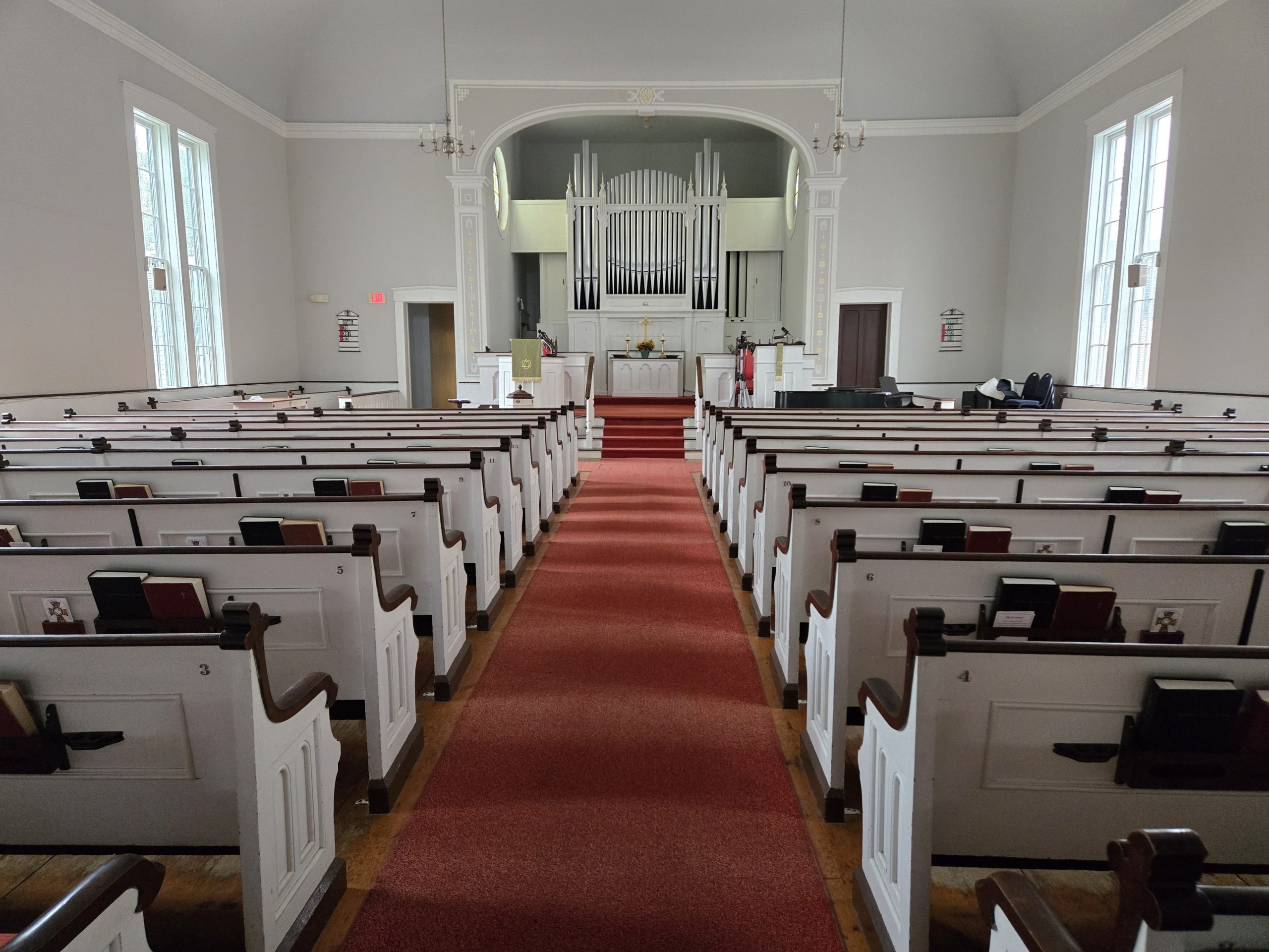Interior of a 1840 new England church displaying white pews and walls and a pipe organ