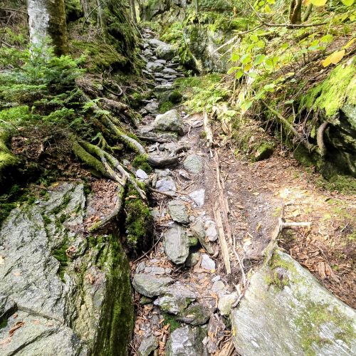 Large rock with a trail walking underneath it on the left over smaller rocks