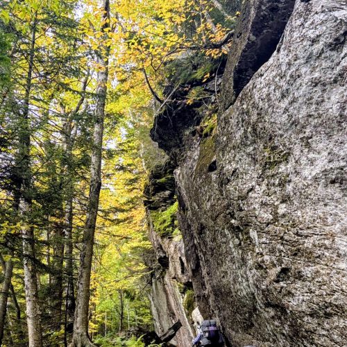 Two backpackers hiking underneath and beside an enormous rock