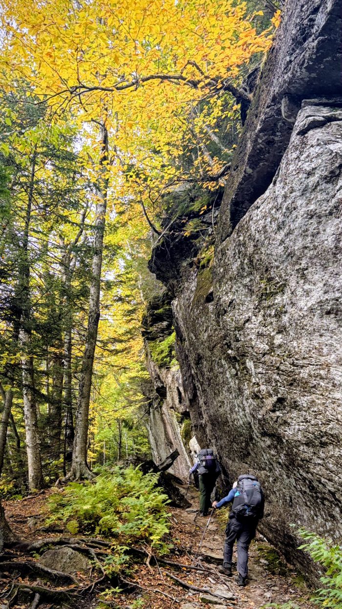 Two backpackers hiking underneath and beside an enormous rock